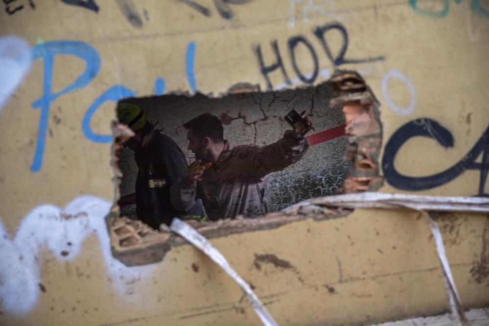 A wall with a small hole broken through it, and a person gesturing on the other side.